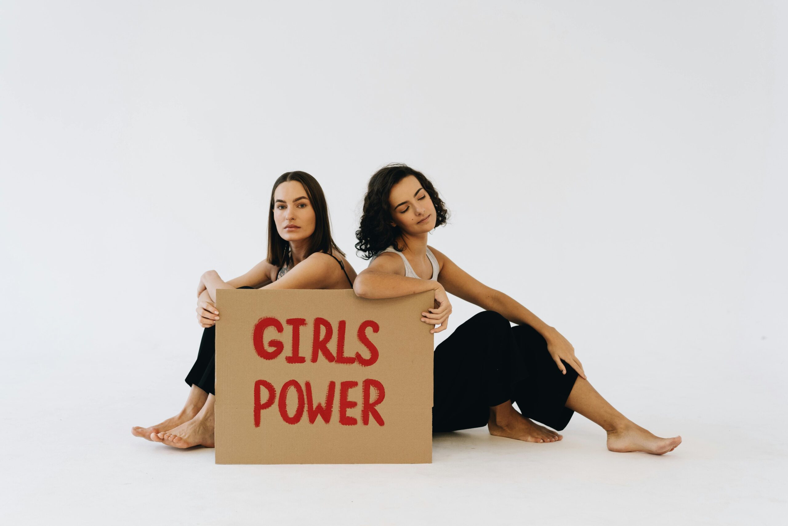Two women sit holding a 'Girls Power' sign, promoting feminism and empowerment.
